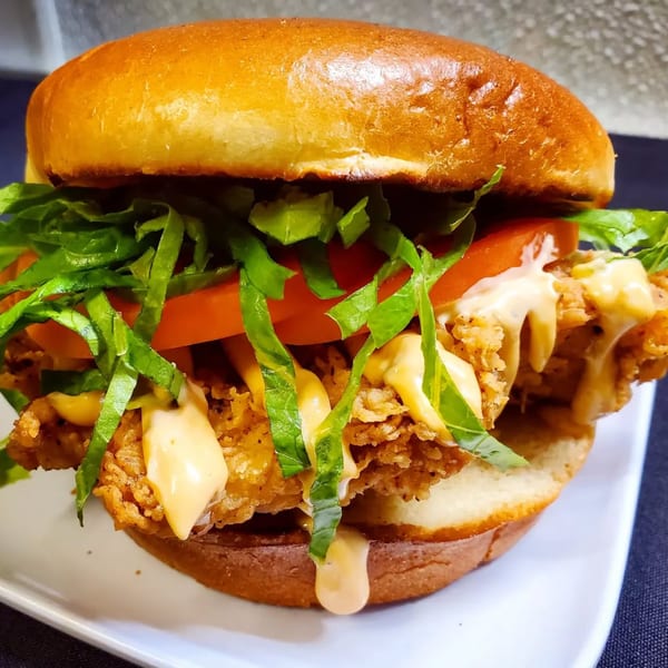A crispy fried chicken sandwich from The Mettle Grill, topped with lettuce, tomato, and special sauce.
