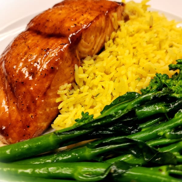 Glazed salmon with yellow rice and green broccoli on a white plate at The Mettle Grill.