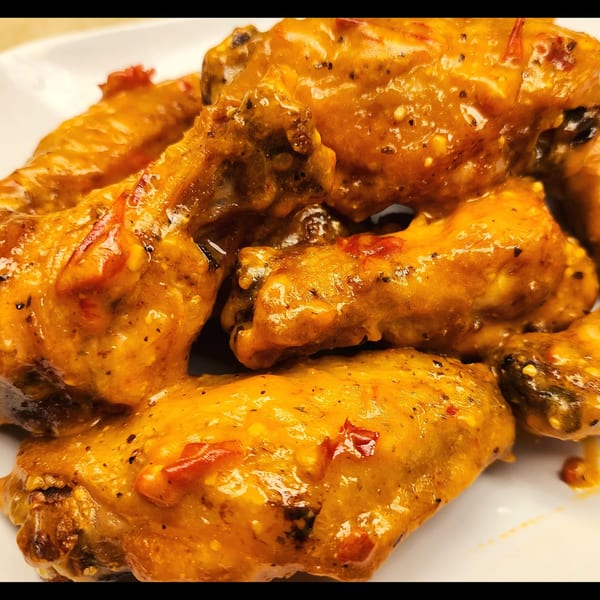 Close-up of Mettle Grill's American-style chicken wings, coated in a rich, orange sauce with visible spices.