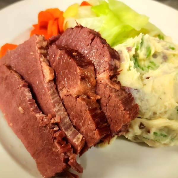 Sliced corned beef with mashed potatoes, carrots, and cabbage on a white plate.