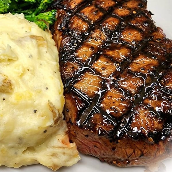 Grilled steak with a dark glaze and grill marks, served alongside mashed potatoes and broccoli.