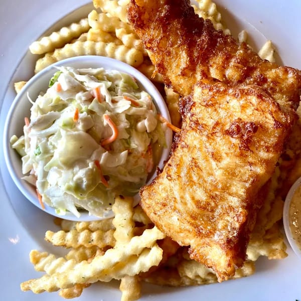 Crispy fried fish with crinkle-cut fries and a side of creamy coleslaw on a white plate.