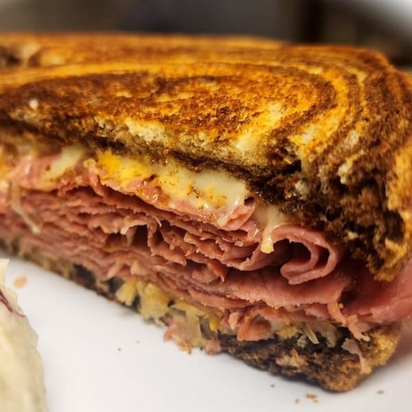 Close-up of a Mettle Grill Reuben sandwich, revealing layers of corned beef, melted cheese, and sauerkraut.